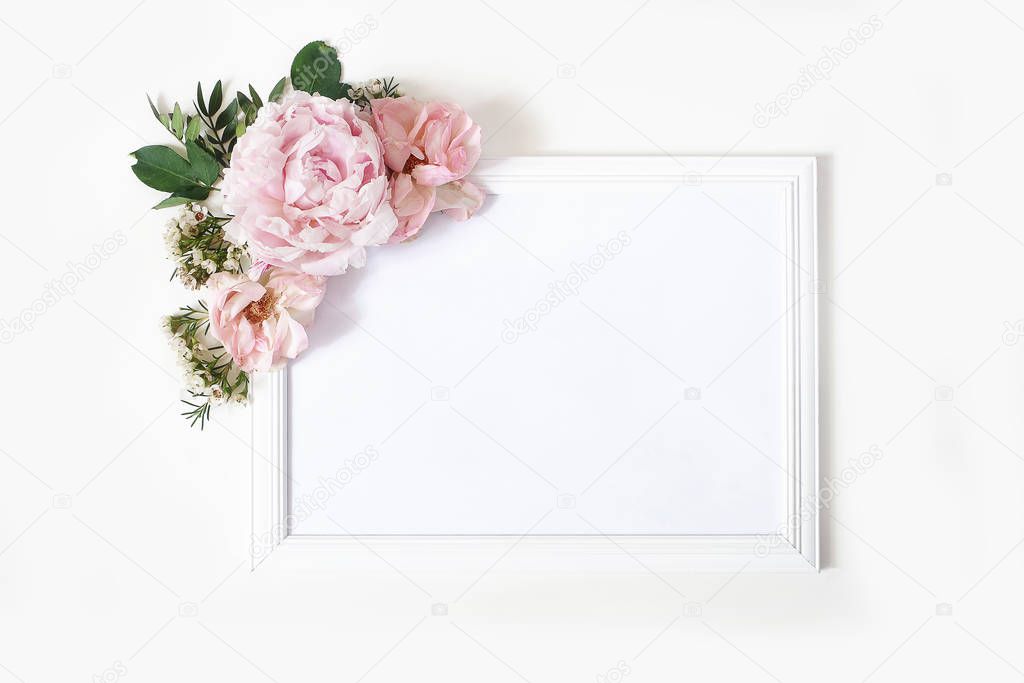 Wedding, birthday sign board mock-up scene. Blank white wooden frame. Decorative floral corner. Green leaves, pink peony, roses and wax flowers. White table background. Flat lay, top view.