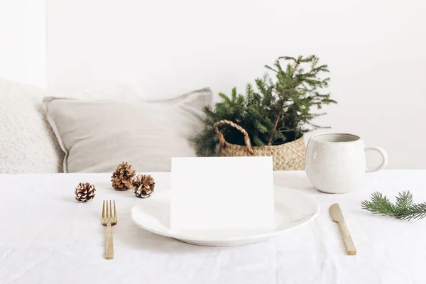 Festliche Weihnachten, winterliche Tischdekoration. goldenes Besteck, Fichtenzweig, Leinentischdecke, Porzellanteller, Tasse Kaffee und Tannenzapfen auf weißem Tischhintergrund. leere Karten-Attrappe. — Stockfoto