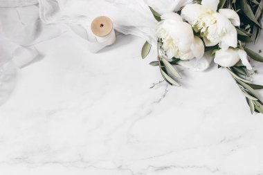 Düğün çiçekleri hala canlı beste yapıyor. Beyaz şakayık çiçekleri, mermer masada zeytin dalları ipek kumaş ve kurdeleli. Klasik kadınsı fotoğraf, düz yatak, üst manzara, insan yok. Boş boşluk