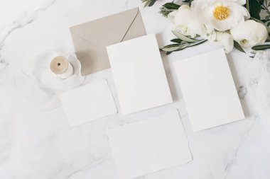 Düğün kırtasiyesi, natürmort beste. Tebrik kartları sahnesi. Beyaz şakayık çiçekleri, zeytin dalları, mermer masada inek maydanozu. Klasik kadınsı fotoğraf, düz yatak, üst manzara.