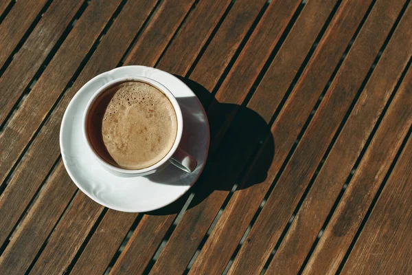 Weiße Tasse Cappucino-Kaffee im Sonnenlicht mit harten Schatten auf altem Holztischhintergrund. Frühstück, Pause. Flach lag, top wetteiferte. Keine Menschen, minimale Zusammensetzung. — Stockfoto
