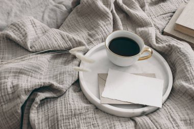 Yatak kırtasiyesinde kahvaltı sahnesi. Bir fincan kahve, boş tebrik kartı, beyaz mermer tepside bir zarf. Muslin atımında kuru Lagurus ovatus yeşilliği. Lifetyle konsepti. Yüksek açı görünümü.