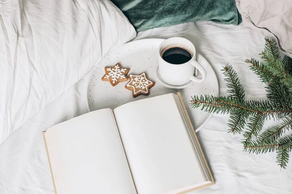 Natura morta festiva di Natale. Libro aperto in bianco, mockup diario con tazza di caffè, biscotti di pan di zenzero e rami di abete rosso su piatto di ceramica. Sfondo vacanza. Colazione a letto. Cuscini in velluto. — Foto Stock