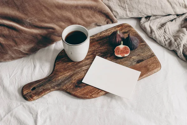 Colazione autunnale nella composizione a letto. Modello di biglietto di auguri in bianco, tazza di caffè e frutta di fico sul tagliere in legno. Sfondo lino bianco. Cuscini di velluto. Ringraziamento, concetto autunnale. Vista dall'alto. — Foto Stock