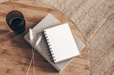 Boş günlük, not defteri modeli ve yuvarlak ahşap masaya kitap. Bir bardak su ve kuru Lagurus ovatus otu. Bulanık bej halı arka planı. Düz yerde, üst tarafta. İskandinav boho iç mimarisi.