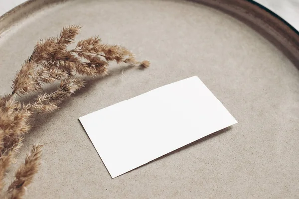 Closeup of blank business card mockup. Dry grass on beige ceramics plate. Fall and Thanksgiving concept. Autumn styled stock still life photo. Selective focus, no people. — Stock Photo, Image