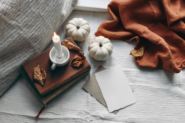 Natura morta d'autunno. Candela accesa, libri e cuscino di lino vicino alla finestra. Scheda di auguri vuota scena mockup. Composizione melmosa con foglie e zucche bianche. Interno scandinavo. Posa piatta, vista dall'alto. — Foto Stock