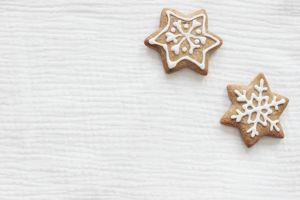 Closeup of star shaped gingerbread cookies with decorative sugar frosting. Christmas cotton muslin fabric mockups scene. Holiday background. Flat lay, top view. Festive still life.