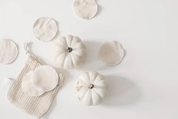 Bio organic cotton reusable round pads for make up removal with pumpkins and knitted bag on white table background. Zero waste concept. Sustainable bathroom and lifestyle. Flat lay, top view. — Stock Photo, Image
