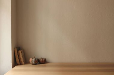 Sonbahar iç kısımları hala hayat dolu. İskandinav oturma odası, ev ofisi. Balkabakları, masada eski kitaplar, masa. Sonbahar, Cadılar Bayramı veya Şükran Günü ev dekorasyonu, boş bej duvar modeli arka plan.