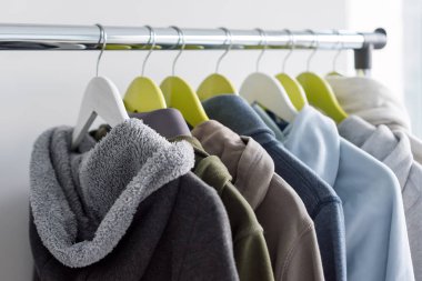 Askı stand bahar ya da gri arka plan üzerinde sonbahar sıcak giysiler ile. Soğuk sezon, rahat kazak ve askı üzerinde hoodie