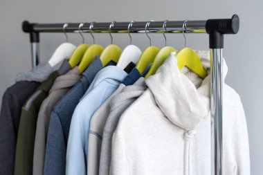 Askı stand bahar ya da gri arka plan üzerinde sonbahar sıcak giysiler ile. Soğuk sezon, rahat kazak ve askı üzerinde hoodie