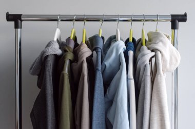 Askı stand bahar ya da gri arka plan üzerinde sonbahar sıcak giysiler ile. Soğuk sezon, rahat kazak ve askı üzerinde hoodie