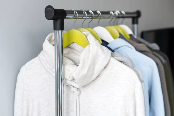 Kleiderbügel mit frühlingshafter oder herbstlicher warmer Kleidung auf grauem Hintergrund. kalte Jahreszeit, kuschelige Pullover und Kapuzenpullover am Kleiderbügel — Stockfoto