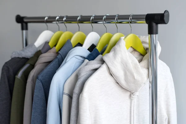 Hanger staan met de lente of herfst warme kleren op grijze achtergrond. Koude seizoen, gezellige truien en hoodie op hangers — Stockfoto