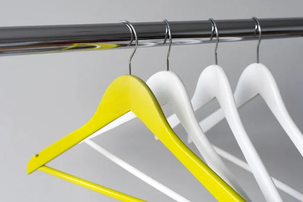 Lege kleerhangers op metalen spoor tegen een grijze achtergrond. Rechthoekig metalen kleding spoor met lege kleur houten kapstokken. — Stockfoto