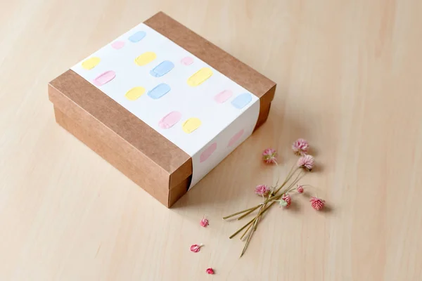 Brown craft paper gift box with dried flowers on wooden table. Selective focus.