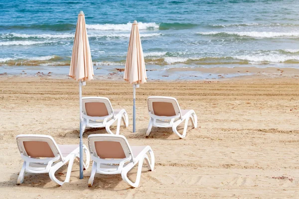 Umbrellas and chaise lounges on the beach. Empty plastic sunbeds near the sea. Tropical vacation, summer background. — Stock Photo, Image