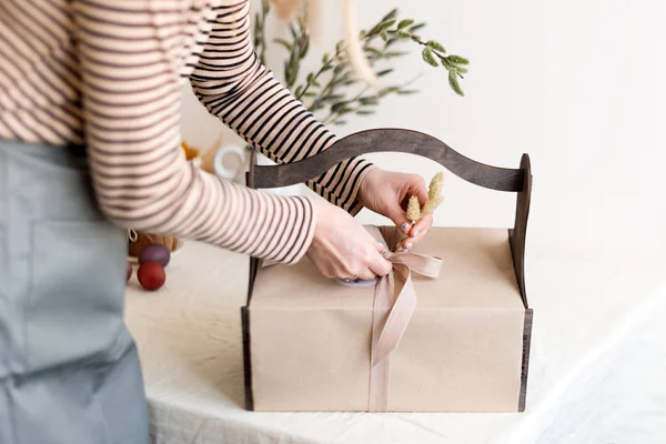 Caja de regalo de madera en manos femeninas con flores de primavera sobre fondo de tela natural claro. Cesta de Pascua con comida tradicional para servir mesa de vacaciones . — Foto de Stock