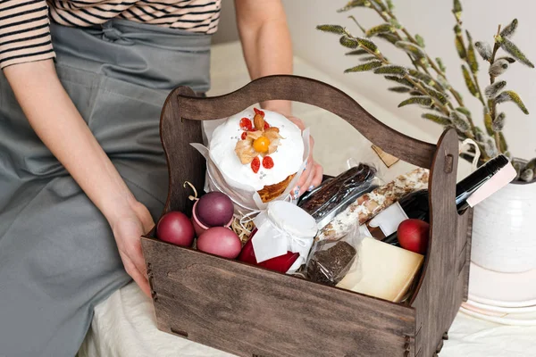 Caja de regalo de madera en manos femeninas con flores de primavera sobre fondo de tela natural claro. Cesta de Pascua con comida tradicional para servir mesa de vacaciones . — Foto de Stock