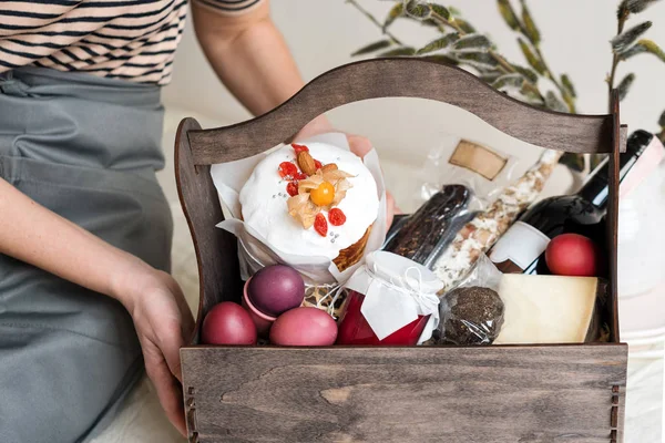 Caja de regalo de madera en manos femeninas con flores de primavera sobre fondo de tela natural claro. Cesta de Pascua con comida tradicional para servir mesa de vacaciones . — Foto de Stock