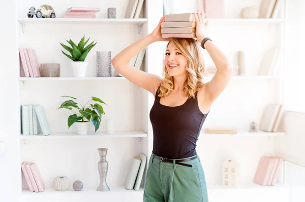 Studentin balanciert Bücher auf dem Kopf. schöne blonde Mädchen hält einen Stapel Bücher auf ihrem Kopf. Bildungskonzept, Kurse, Prüfungen, Hausaufgaben, Liste der zu lesenden Bücher. — Stockfoto