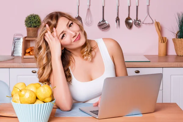 Orolig och ledsen elev kvinnlig söker information i en bärbar dator på nätet sitter i köket. Ledsen blond kvinna känner sig stressad på grund av ekonomiska problem, att arbeta genom finanser Stockbild