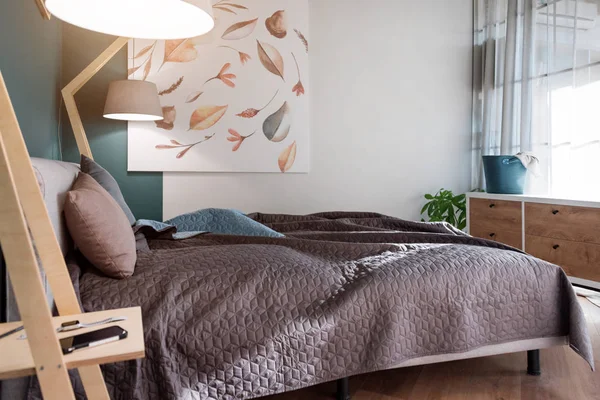 Close-up van een bed met gekleurde kussens, Bedspread en een gezellige lamp. Tijdschrift op tafel, avond lezen. Loft interieur, minimalistische Scandinavische stijl. — Stockfoto