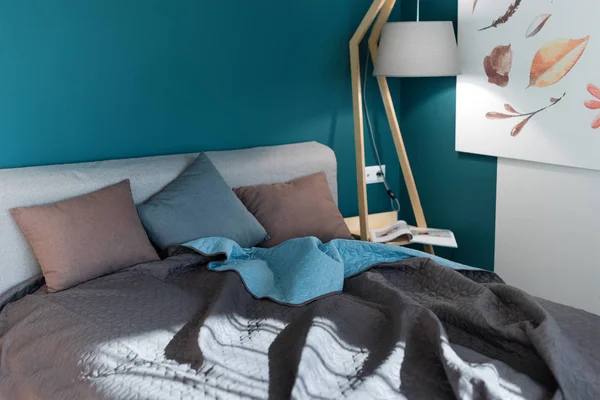 Close-up van een bed met gekleurde kussens, Bedspread en een gezellige lamp. Tijdschrift op tafel, avond lezen. Loft interieur, minimalistische Scandinavische stijl. — Stockfoto