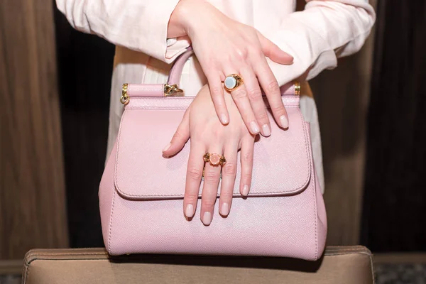 Manos de mujer con manicura y anillos de joyas de lujo. Primer plano de la bolsa de cuero rosa de moda con las manos femeninas que muestran joyas de moda en la cámara. Concepto de manicura y moda . — Foto de Stock