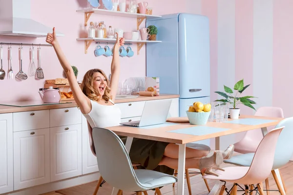 Lächelnde junge Frau mit Laptop in der Küche zu Hause. Blondine arbeitet am Computer, Freelancer oder Bloggerin zu Hause — Stockfoto