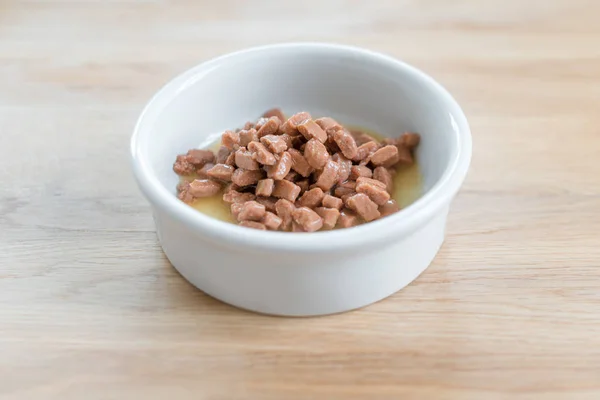 Natte voeding voor katten en honden in een witte kom op houten vloer close-up — Stockfoto