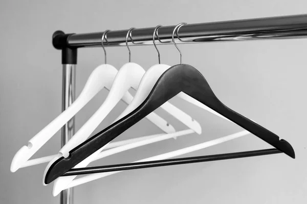 Empty clothes hangers on metal rail against grey background. Rectangular metal clothing rail with empty white and black wooden coat hangers. — Stock Photo, Image