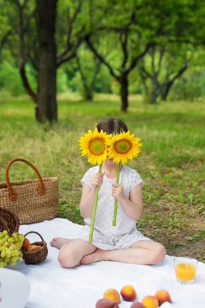 Girl holding sunflower in front of face outdoors. Outdoor party in the garden, picnic. — Stock Photo, Image