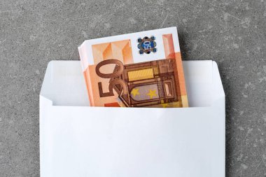 50 Euro 'luk banknotlarla dolu beyaz bir zarf. Elli avroluk banknotlar dolusu açık posta zarfları betonun üzerinde. Hediye olarak zarfa katlanmış bir avroluk banknot. Para göndermek veya biriktirmek, yolsuzluk kavramı.