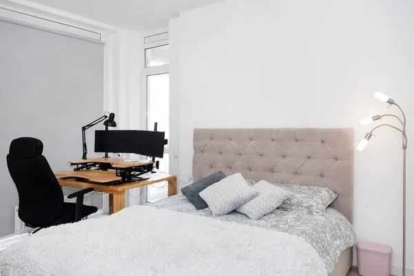 Bedroom interior with a study corner. Large double bed and a desk with a computer and a rolling chair. Home office, freelance work. — Stock Photo, Image