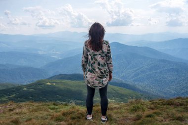 Dağlarda yalnız gezen bir kız, sakin bir manzara. Dışarıda yürüyüş, dağın tepesinde kadın yürüyüşçü. Manzaranın arka görüntüsü. Yolculuk teması. Karpat Dağları, Ukrayna 'nın Hoverla Dağı manzarası