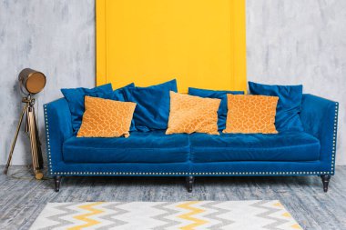 Basit minimalist bir dairede turuncu yastıklı rahat bir mavi kanepe. Oturma odası iç dekorasyonu..