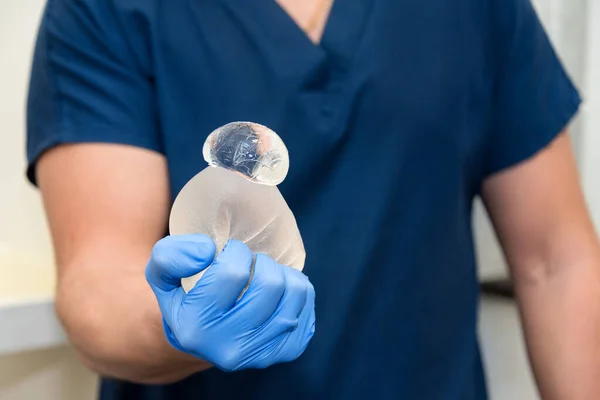 Damaged torn gummy bear breast implant in surgeon's hands. Demonstration of the reliability of the breast implant, it is damaged, but the gel remains inside it. Risks of breast implant surgery. — Stock Photo, Image