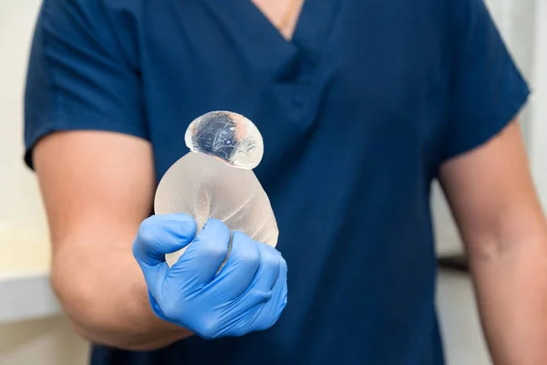 Zerrissene Gummibärchen-Brustimplantate in den Händen des Chirurgen. Demonstration der Zuverlässigkeit des Brustimplantats, es ist beschädigt, aber das Gel bleibt darin. Risiken einer Brustimplantat-Operation. — Stockfoto