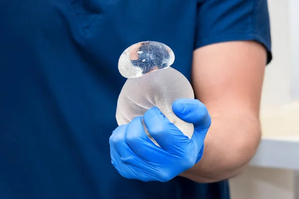 Hasarlı parçalanmış sakızlı ayı göğüs implantı cerrahın ellerinde. Göğüs implantının güvenilirliğinin kanıtı, hasar görmüş, ama jel içinde kalmış. Göğüs implantı ameliyatı riski.