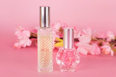 Farklı şeffaf parfüm şişeleri ve pembe arka planda çiçek açan ağaç dalları. Kiraz çiçekli Aromatik esans şişeleri. Parfüm, kozmetik, parfüm koleksiyonu.