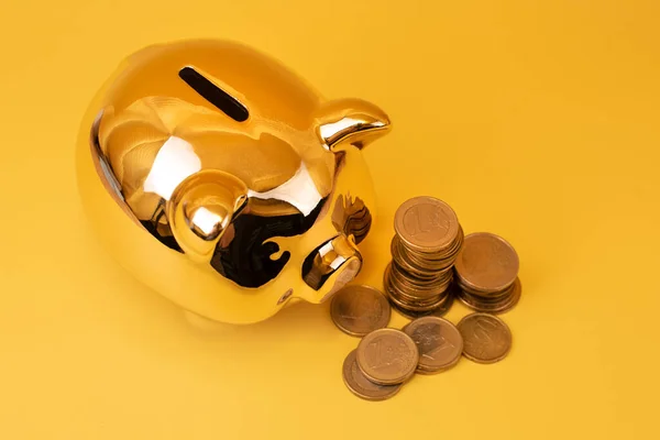 Golden piggy bank with money towers on yellow background. Stack of euro coins near golden money box. Money pig, money saving, moneybox, finance and investments concept. Free space for text.