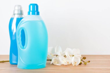 Deterjan şişeleri ve ahşap masa üzerinde orkide çiçekleri olan yumuşatıcı. Konteynırlar dolusu temizlik ürünleri, ev yapımı kimyasallar. Sıvı deterjan ve krem. Çamaşır günü, temizlik konsepti