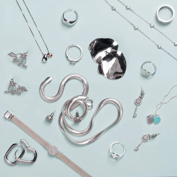 Minimum mavi arka planda gümüş mücevherler. Yüzükler, bilezikler ve küpeler. Moda kadını aksesuarlarının, mücevherlerin ve alışveriş konseptinin en üst görüntüsü. Moda minimalist geometrik düz konum. — Stok fotoğraf