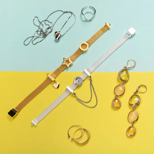 Asgari sarı ve mavi arkaplanda gümüş ve altın mücevherler. Yüzükler, bilezikler, küpeler ve kolye. Lüks kadın aksesuarlarının, mücevherlerin ve alışveriş konseptinin en üst görüntüsü. Düz konum