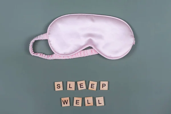 Words SLEEP WELL and pink sleeping eye mask, top view. Good night, flight and travel concept. Sweet dreams, relax, siesta, insomnia, relaxation, tired, travel concept. Do not disturb, bedtime concept.