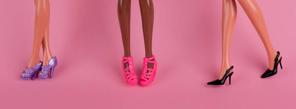 Doll legs in stylish heel shoes. Legs of dolls representing different races on pink background. The concept of female friendship, fashion and beauty