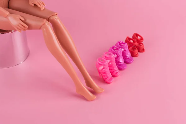 プラスチック製のおもちゃの人形とピンクの背景にスタイリッシュな靴の長いスキニー足 女性は新しい靴を選択し どのペアを購入するかを決定します ファッションとショッピングのコンセプト — ストック写真
