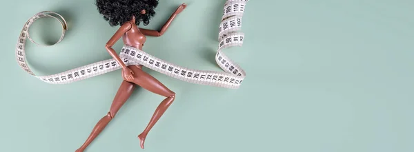 Doll wrapped in measuring tape. Tied up unrecognizable plastic doll, weight loss, fasting and slimming, diet, anorexia, overeating control, female fight for perfect fit body concept. Free copyspace — Stock Photo, Image